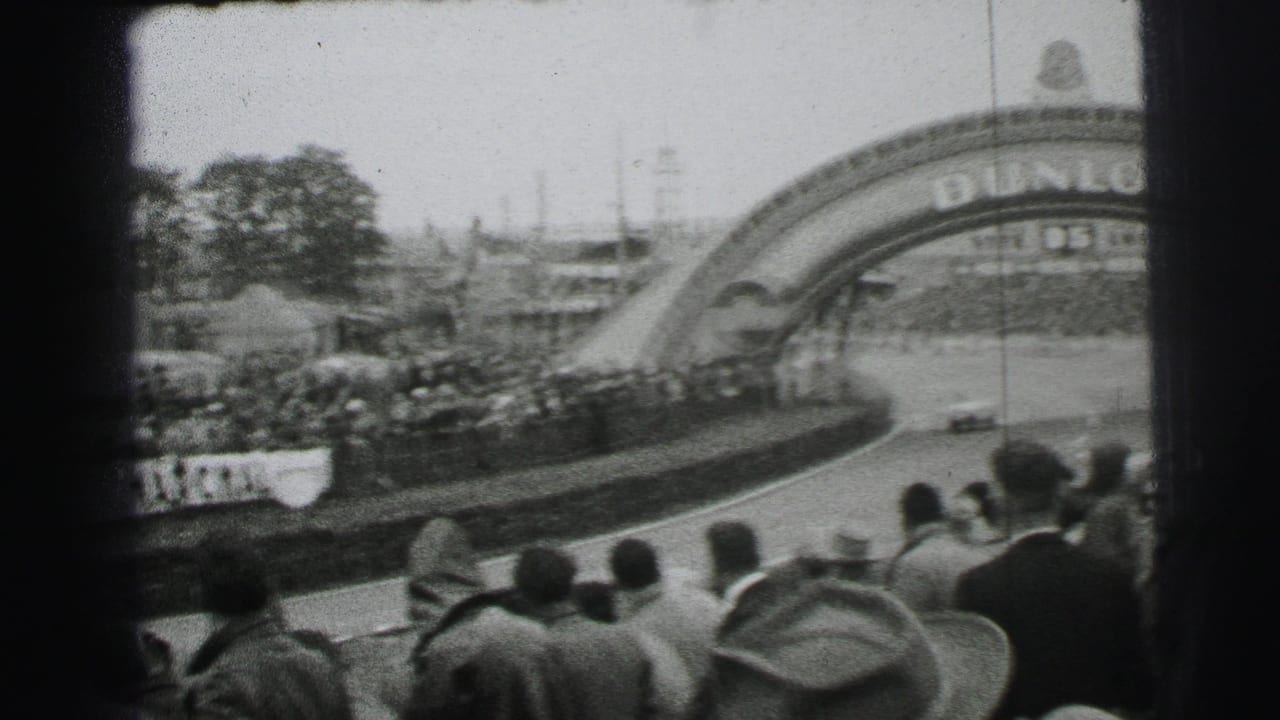 1954 Le Mans 8mm frame with cars on the circuit below the Dunlop bridge and a dense spectator crowd in the foreground.