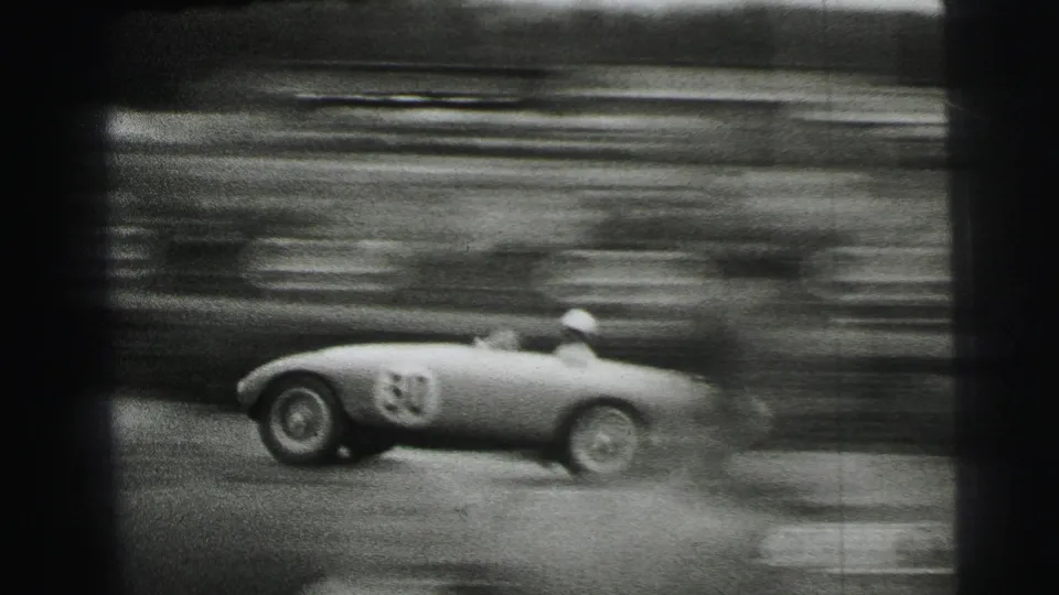 A light-colored open race car, marked with a visible number, passes quickly on the Le Mans circuit with strong motion blur.