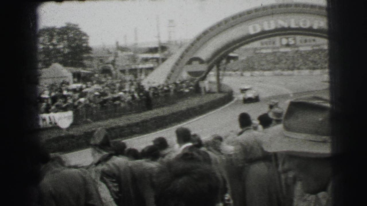 Spectators watch a racing car approach a bend beneath a Dunlop arch.