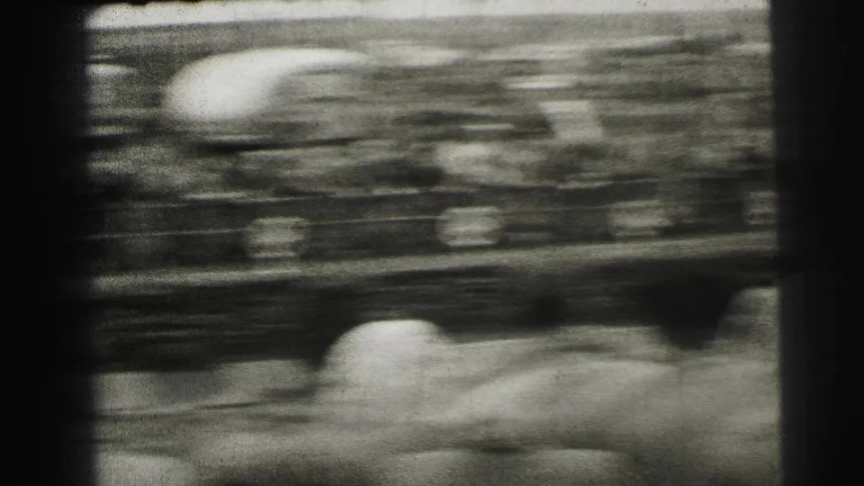 Blurred 8mm frame from Le Mans showing a racing car passing close to trackside spectators, with motion streaks across the scene.