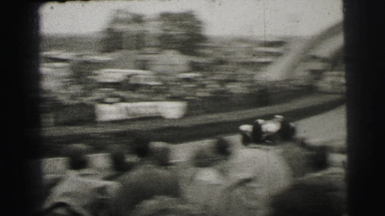 Handheld 1954 Le Mans frame with a blurred racing car, trackside spectators, barriers, and part of the Dunlop arch at the edge.