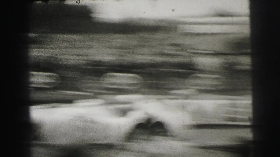 A race car blurs past spectators at Le Mans in 1954, seen from a handheld 8mm crowd viewpoint.
