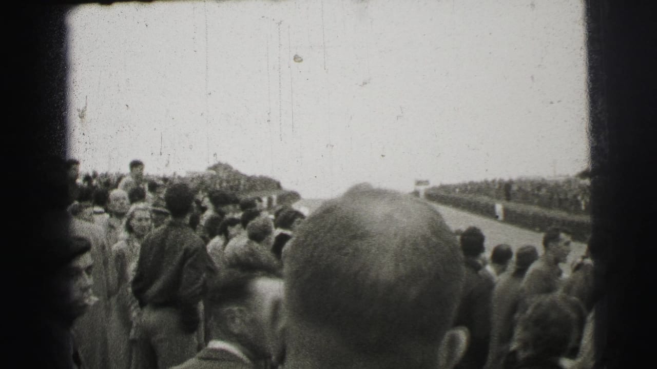 Crowd members in mid-century dress watch the Le Mans circuit from a trackside vantage point in 1954.