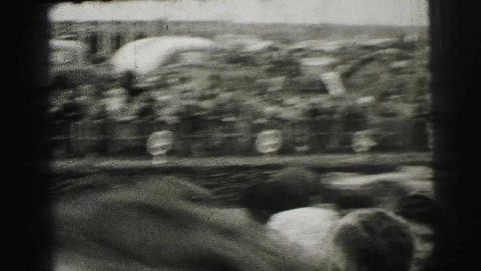 A race car flashes past a dense Le Mans crowd, captured with heavy motion blur on 8mm film.