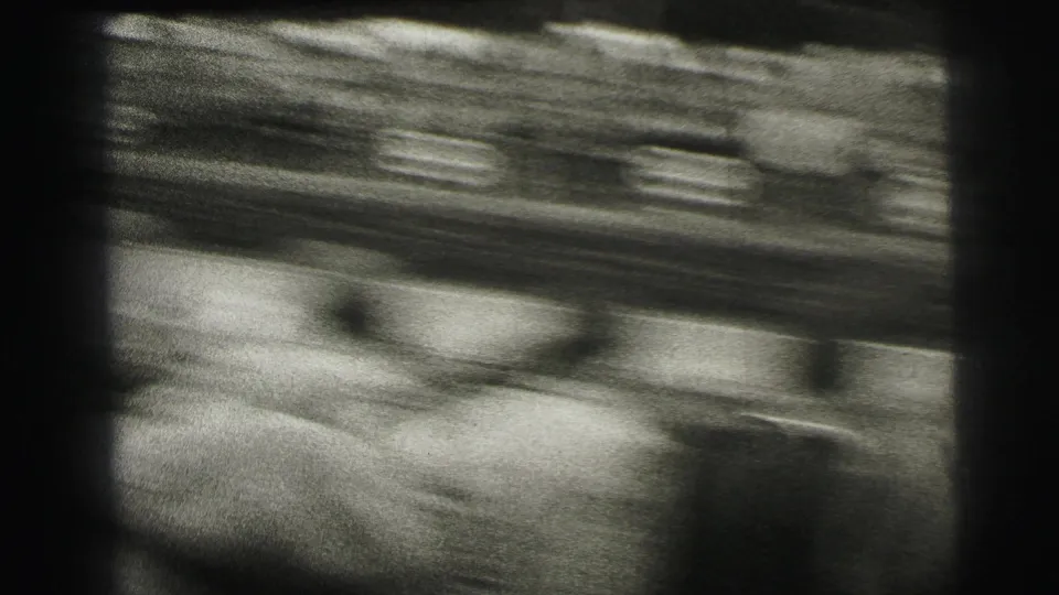 A blurred black-and-white 8mm view of a race car moving past spectators at Le Mans, France, consistent with the supplied 1954 metadata.