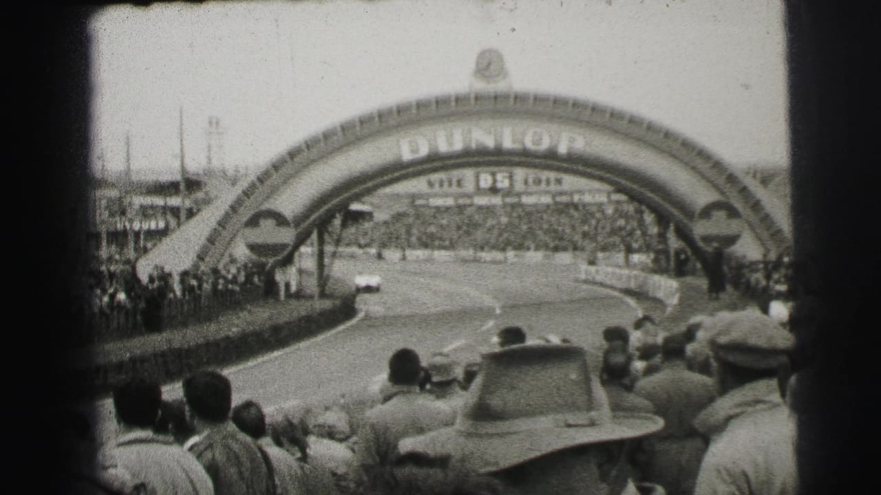 Crowds line the Le Mans circuit as race cars approach the Dunlop arch, with grandstands and track barriers visible in black-and-white 8mm footage.
