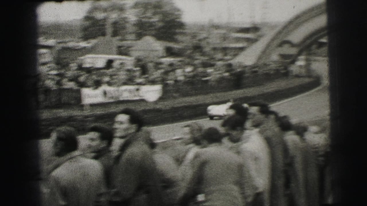 1954 Le Mans crowd view with spectators in mid-century dress watching a small racing car near the Dunlop arch area.