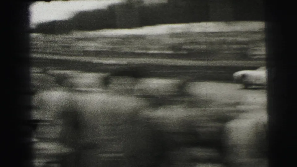 Black-and-white 8mm frame from Le Mans showing racing cars blurred by speed as they pass along the track.