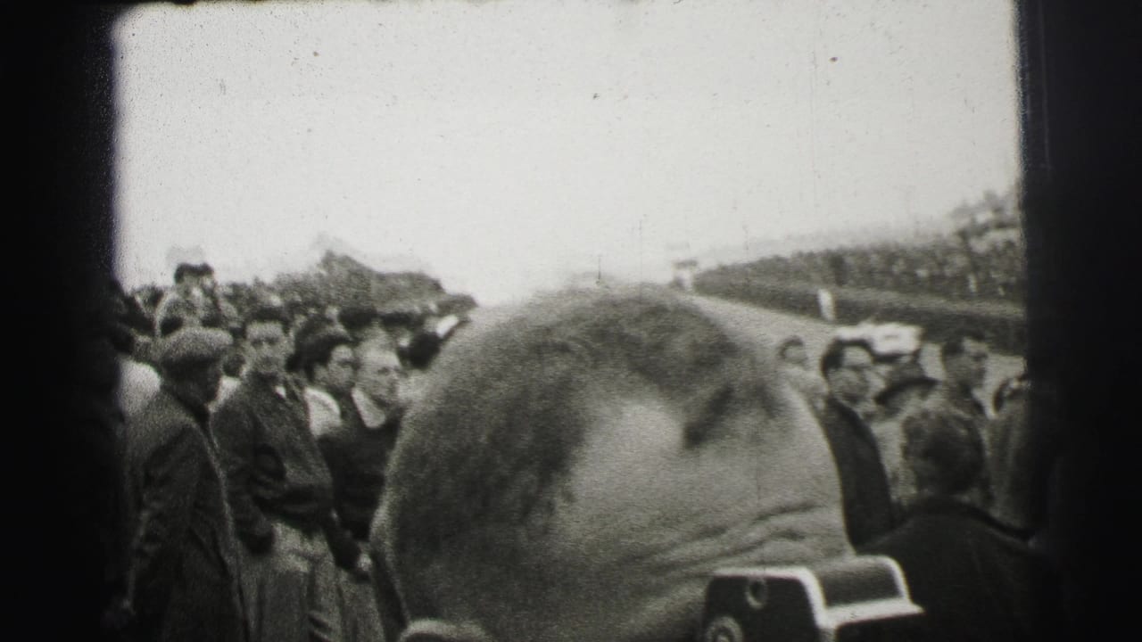 Crowd beside a race track with a spectator head blocking the lower foreground.