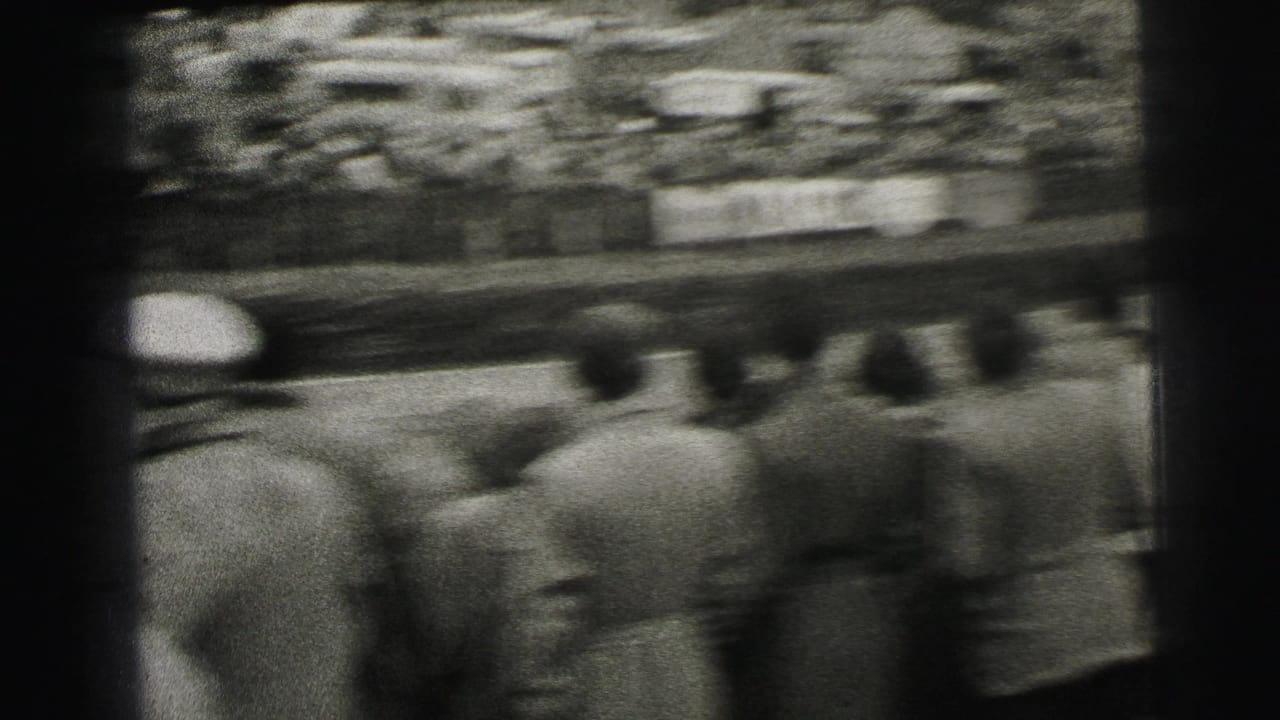 A race car streaks past the Le Mans crowd, with motion blur and spectators seen from behind near the circuit edge.
