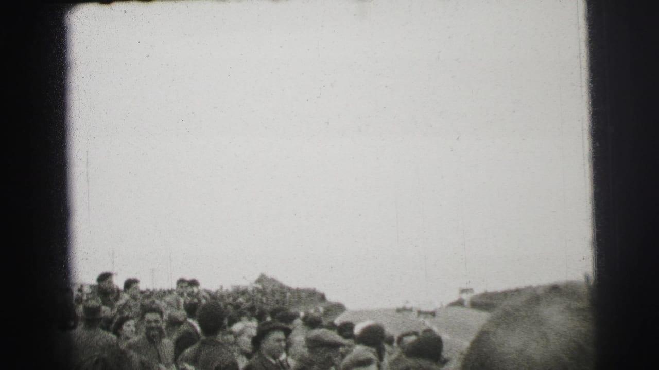 A dense Le Mans crowd watches from beside the course, with foreground heads and distant spectators visible in the 8mm frame.