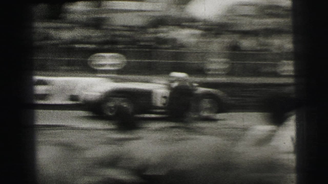 A race car blurs through the frame at Le Mans, emphasizing speed as spectators watch from behind the course edge.