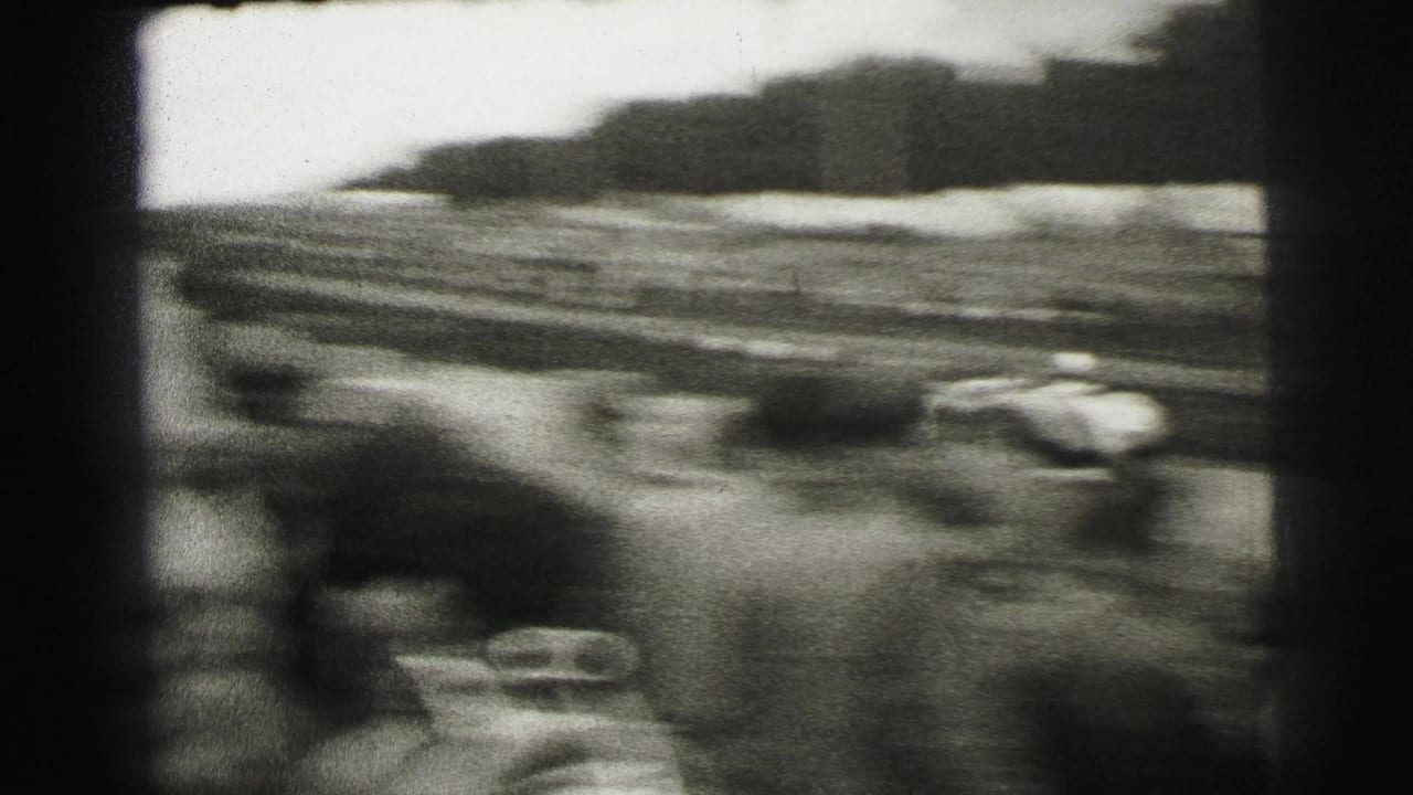 A blurred race car speeds past trackside spectators in 1954 Le Mans 8mm footage.