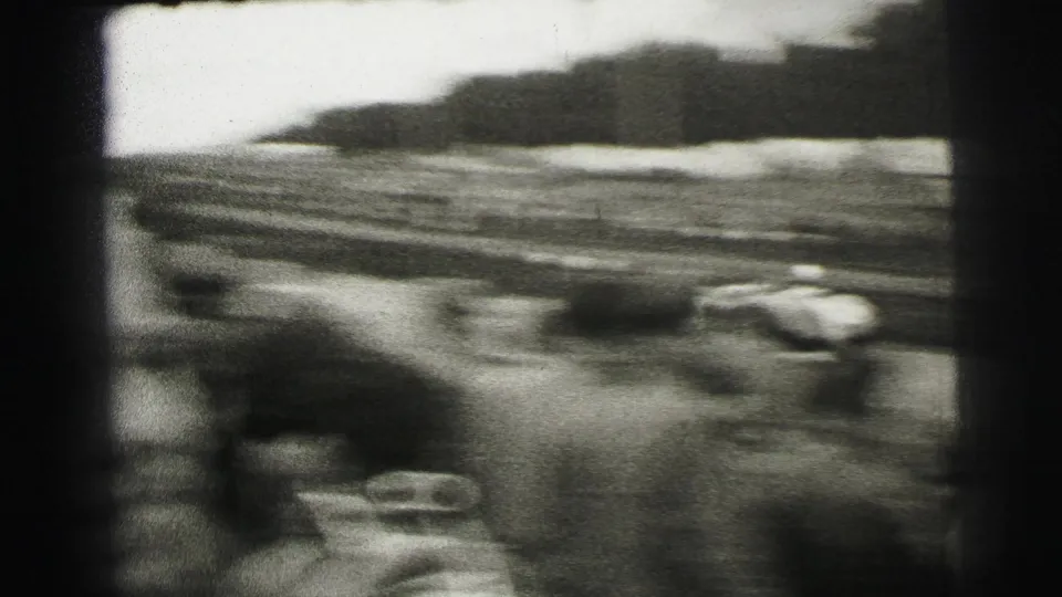 A blurred race car speeds past trackside spectators in 1954 Le Mans 8mm footage.