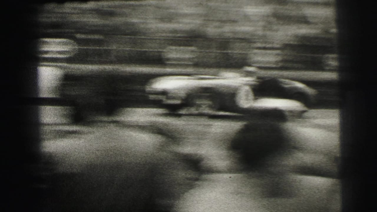 A low race car blurs across the frame with a packed Le Mans spectator area behind it.