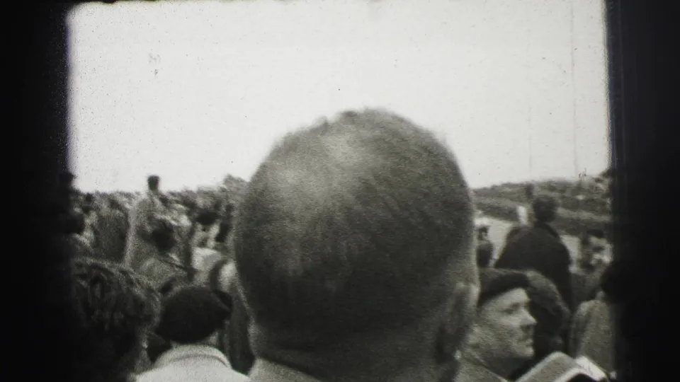 Le Mans spectators viewed from behind, with a bald head in the foreground and the course visible beyond the crowd.