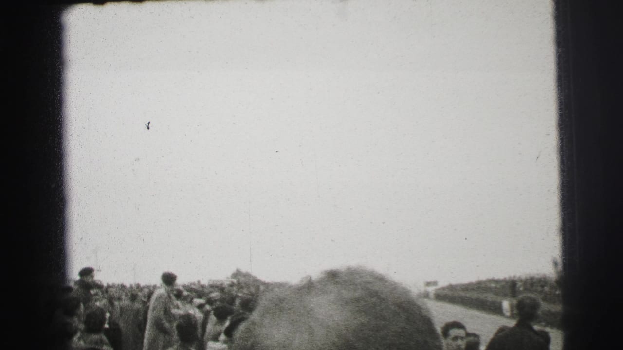 Crowd gathered beside a race track under a bright sky.