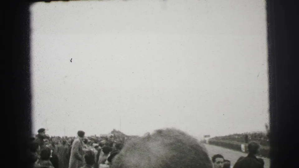 Trackside spectators at Le Mans in 1954 watch from beside the circuit in grainy black-and-white 8mm footage.