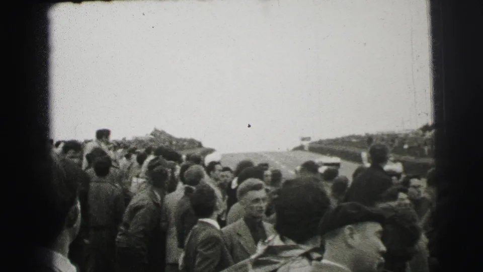 Crowded Le Mans trackside scene from 1954, with spectators in coats and caps watching the course from close range.