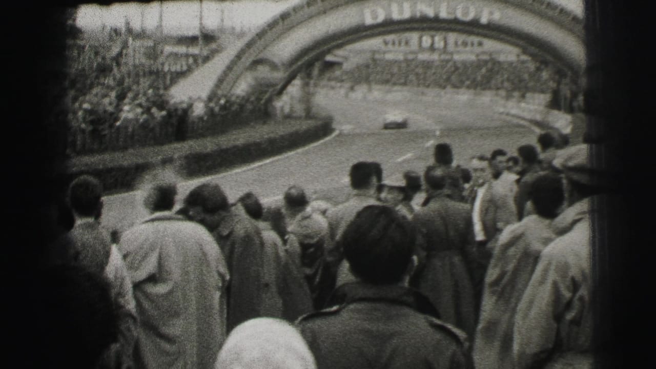 Spectators at the Le Mans circuit watch cars move through a bend beneath the visible Dunlop arch.