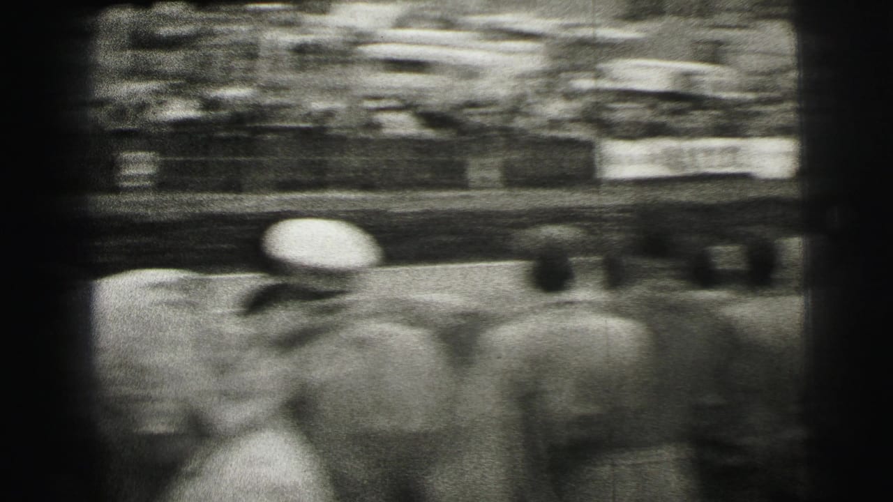 The camera swings past spectators near the Le Mans track, creating a blurred home-movie view of the crowd and racing area.
