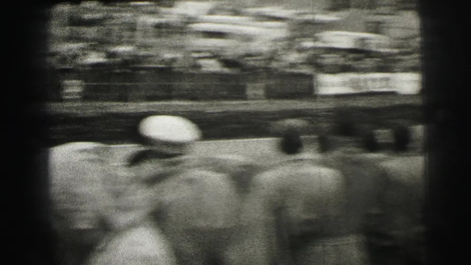 The camera swings past spectators near the Le Mans track, creating a blurred home-movie view of the crowd and racing area.