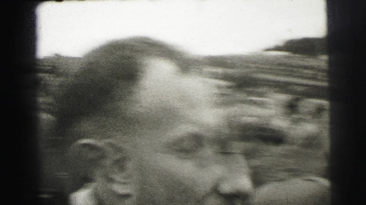 A close spectator profile fills the foreground as the Le Mans track and viewing crowd blur behind him.