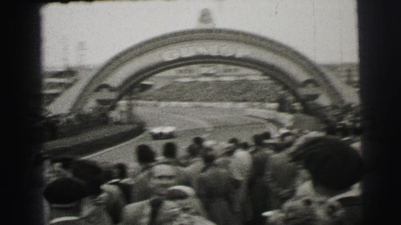 Spectators face a racecourse with a large arched structure visible across the track.