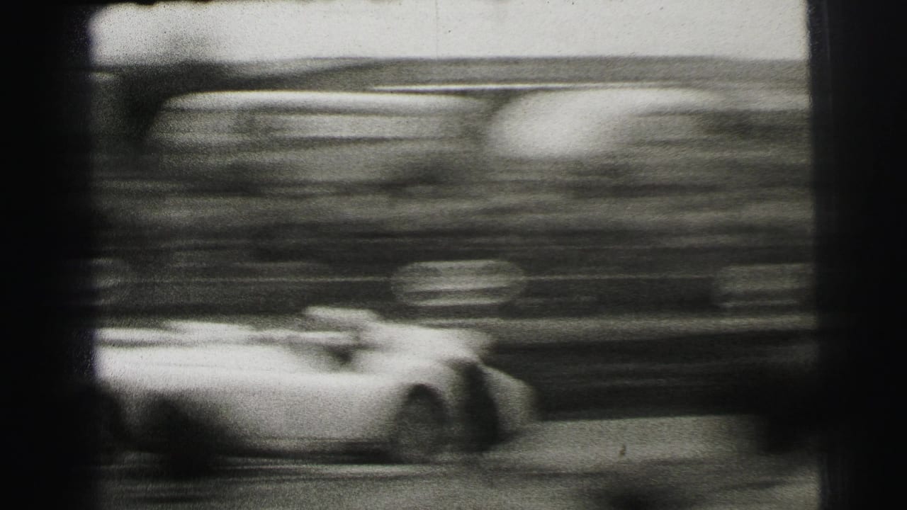 A fast race car blurs past the Le Mans crowd, emphasizing speed in grainy black-and-white 8mm footage.