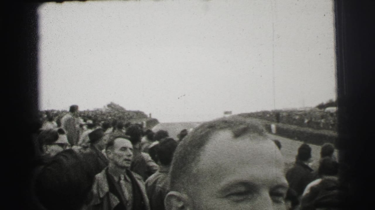 Le Mans spectators stand along the track as a foreground man's face and head partially obscure the home-movie view.