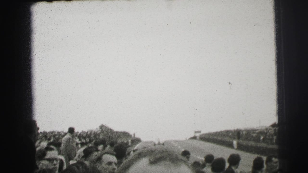 1954 Le Mans home-movie frame showing spectators beside a road circuit as the track stretches away into the distance.