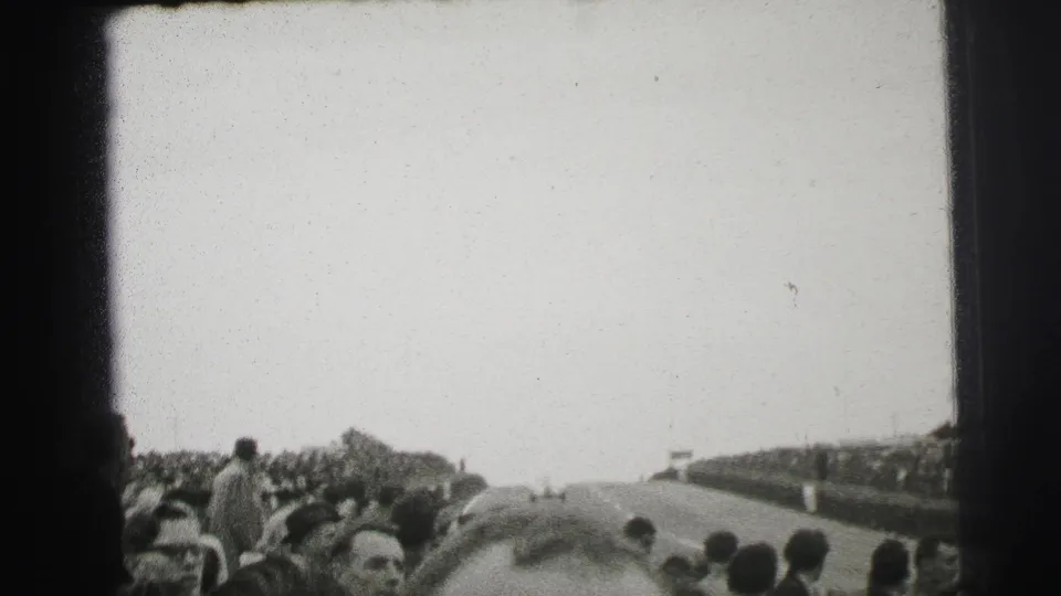 1954 Le Mans home-movie frame showing spectators beside a road circuit as the track stretches away into the distance.
