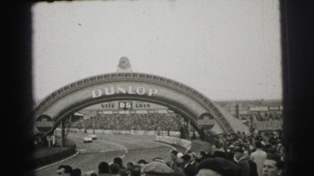 Race cars approach beneath the Dunlop arch with spectators packed along both sides.
