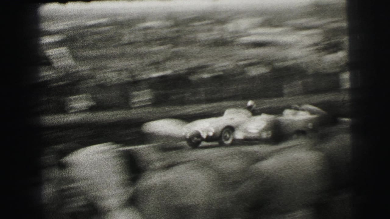 1954 Le Mans frame with strong motion blur as race cars pass close to the spectator area in black-and-white 8mm footage.