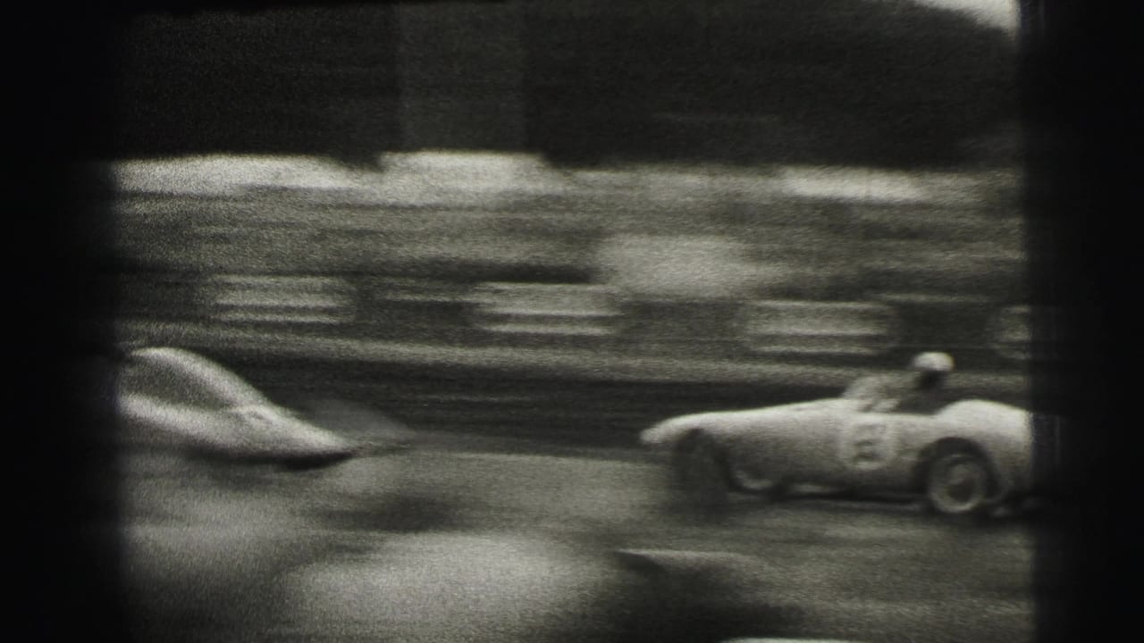 Black-and-white 8mm frame from Le Mans showing a blurred race car, number 63, speeding past a spectator-lined track.