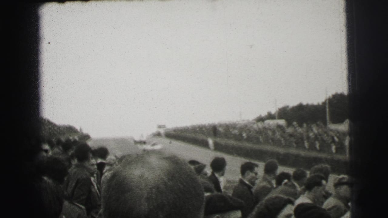 1954 Le Mans spectator view with a distant race car on the track and crowds lining the roadside barriers.