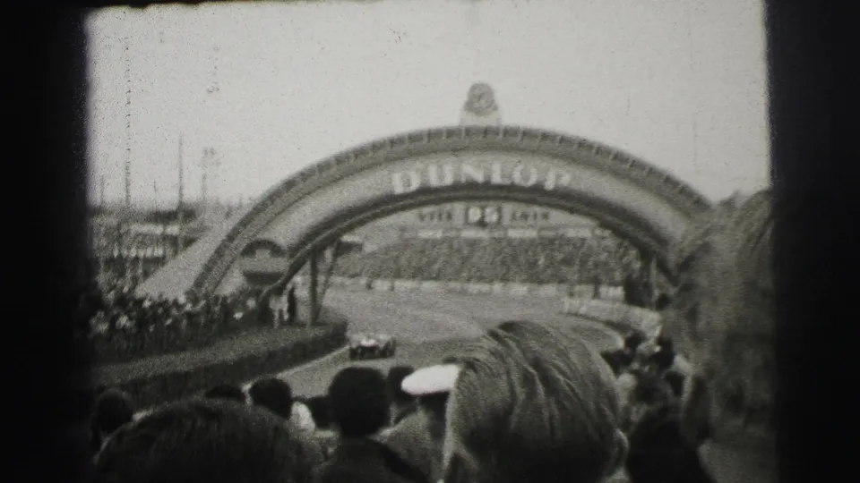 The Dunlop bridge at Le Mans spans the circuit as spectators watch from the foreground and trackside areas.