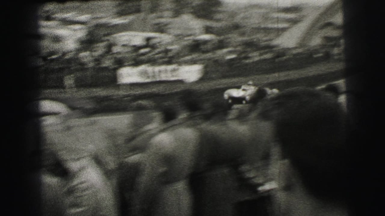 Blurred race car passes spectators along a crowded track edge.