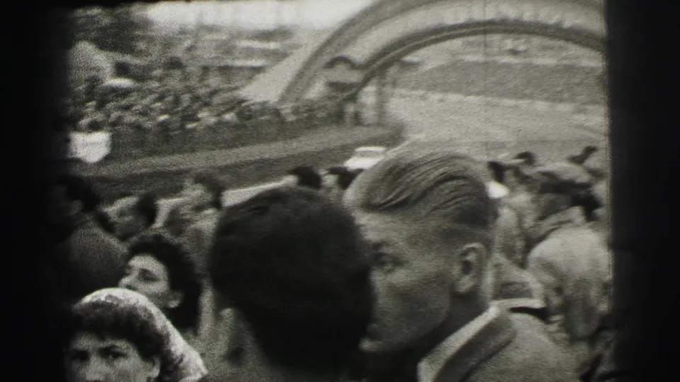 Trackside 1954 Le Mans home-movie view of spectators packed near the Dunlop arch, with several faces close to camera.