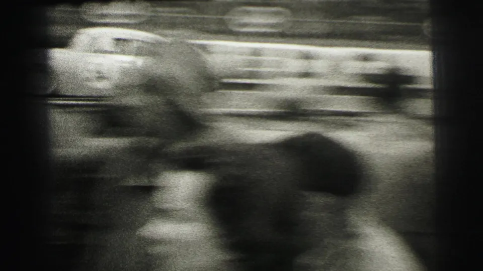 A race car streaks past in motion blur at 1954 Le Mans, filmed from behind spectators near the track.