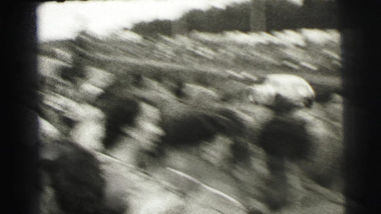 Black-and-white 8mm frame from Le Mans showing a blurred trackside crowd as a race car passes during the event.