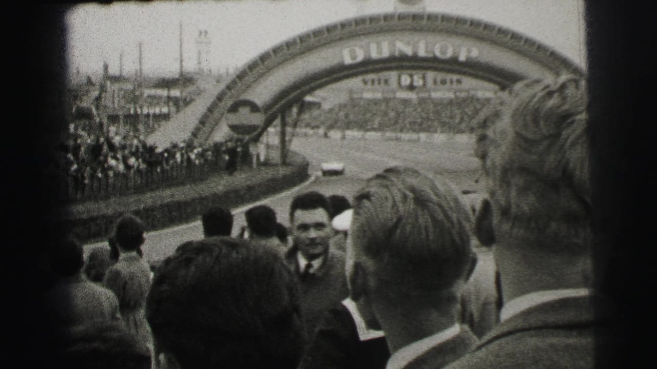 Le Mans trackside spectators face the course near the Dunlop bridge, with a race car visible on the straightaway.