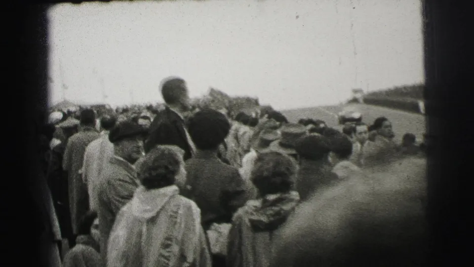 1954 Le Mans home-movie view of spectators in coats and hats gathered beside the racetrack.