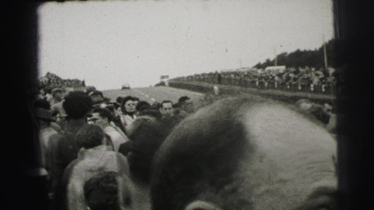 Spectators line a curving racetrack, with a person's head close to the camera.