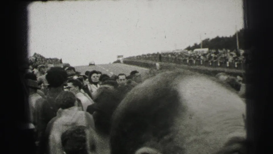 Le Mans racetrack crowd seen from within the spectators, with the course curving away in the background.