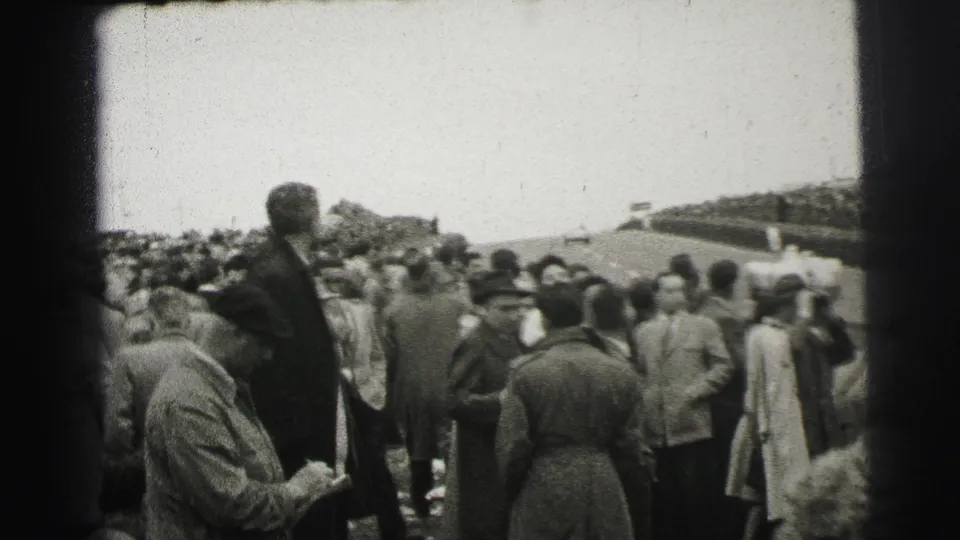 1954 Le Mans crowd scene with spectators gathered shoulder-to-shoulder near the course and a distant banner-like feature.