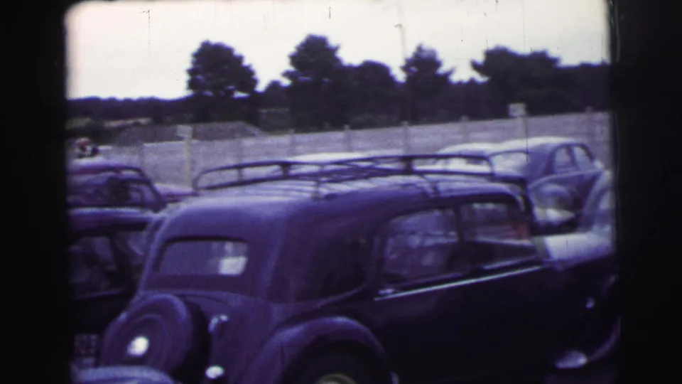 A dark vintage saloon with a roof rack appears in a row of cars during the 1954 Le Mans home-movie scene.