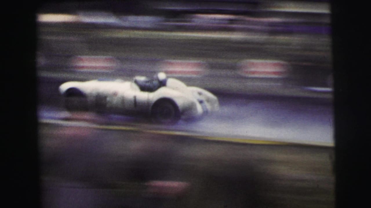 At Le Mans in 1954, a white open race car passes on a rain-dark track with strong motion blur and dark film edges.