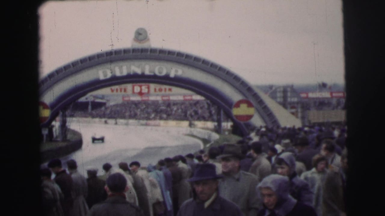 1954 Le Mans crowd scene with spectators in coats watching cars move beneath the large Dunlop bridge over the circuit.