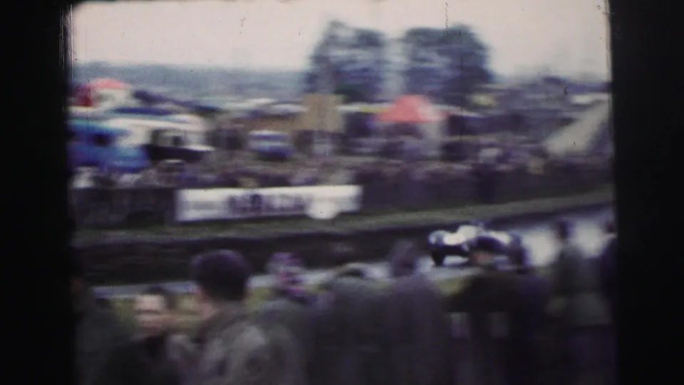Soft, motion-blurred 1954 Le Mans frame with a race car passing in front of spectators, barriers, trees, and trackside signs.